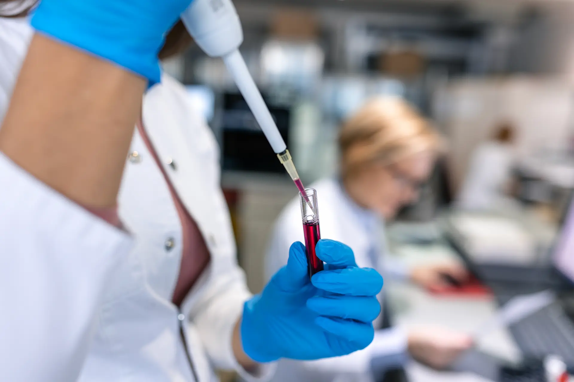 Tecnico di laboratorio con guanti blu preleva del liquido con una pipetta da una provetta per analisi del sangue nel centro medico