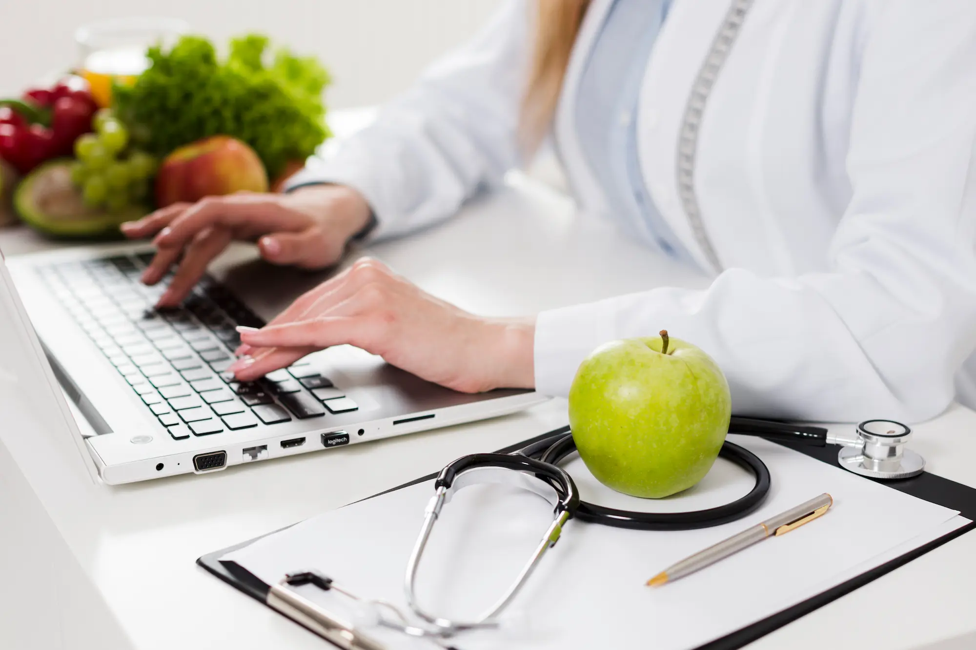 Nutrizionista con camice medico prepara una dieta personalizzata al laptop con frutta e verdura sullo sfondo nel centro