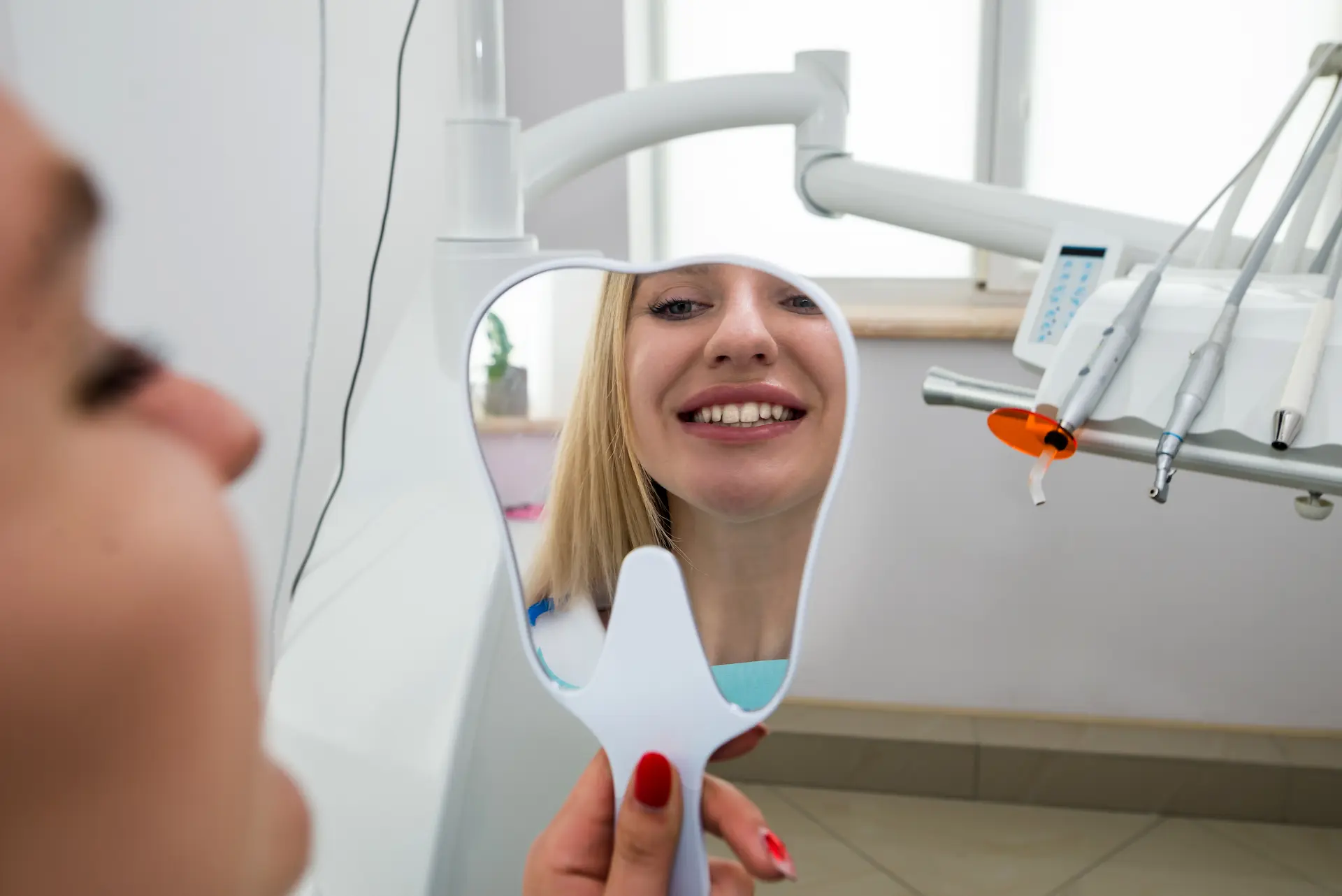 Paziente femminile sorridente si guarda nello specchio dopo un trattamento di sbiancamento dentale nel centro