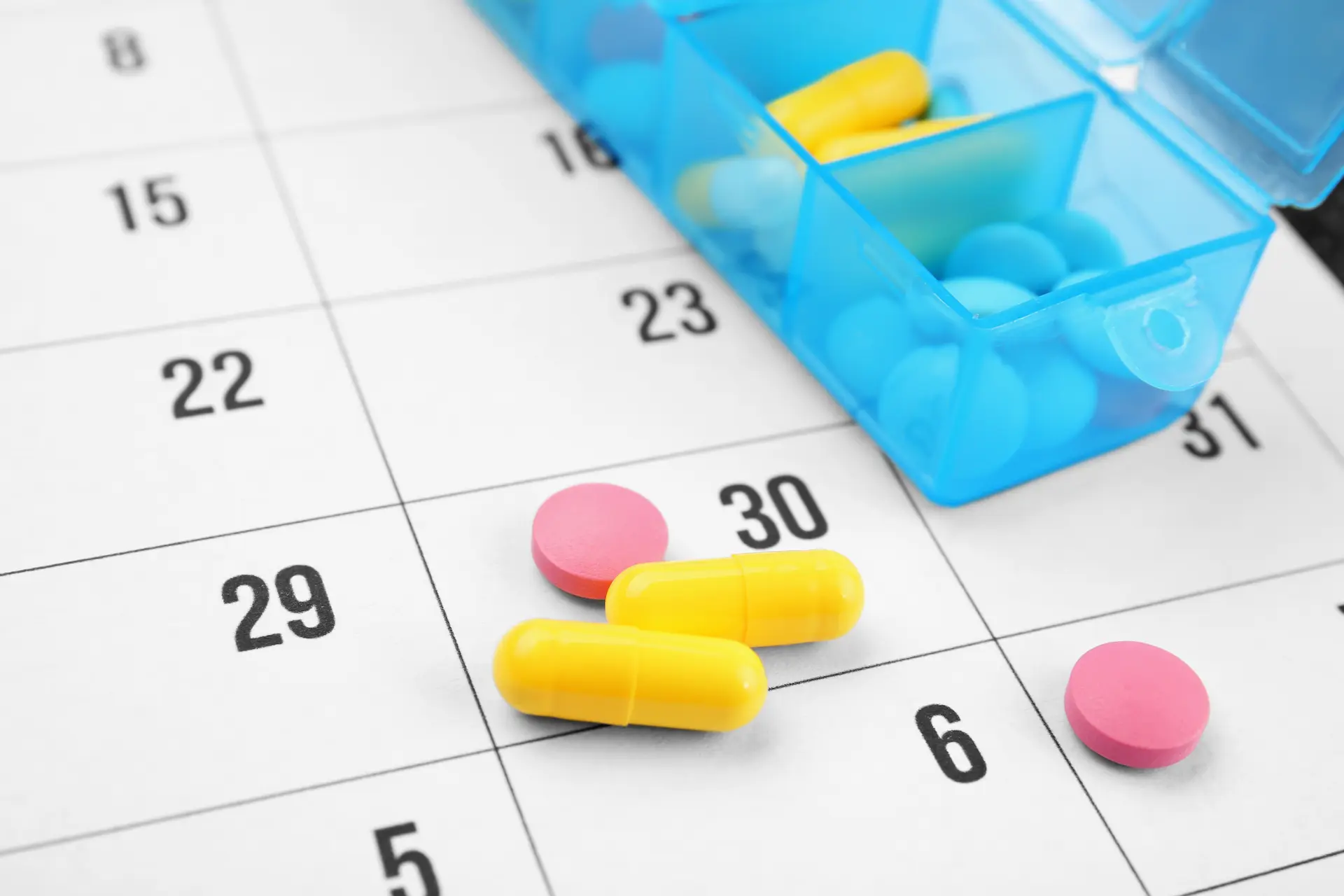 Pillole e farmaci in un portapillole settimanale posizionato su un calendario per ricordare il piano terapeutico nel centro medico